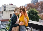 Lesbian couple relaxing and drinking wine on apartment's balcony