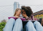 two young women laugh together as they study, and discuss why their zodiac signs will be the luckies...